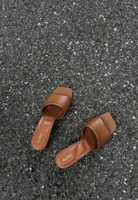 Bruine schuifsandalen van glad synthetisch materiaal, met een vierkante neus en een brede band. Logo bedrukt op de binnenzool.