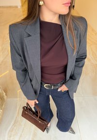 Blazer en tartan gris, haut bordeaux foncé, jeans en denim foncé évasés, sac à main en daim marron et talons imprimé serpent. Des boucles d'oreilles dorées ajoutent une touche de détail.