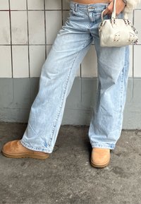 Hele sinised laiapidised teksapüksid tuhmunud teksatuurega, kombineeritud helepruunide seemisnahast saapade ja väikese valge käekotiga, millel on dekoratiivsed detailid.