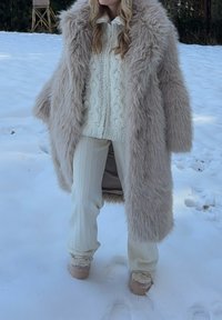 Valge beeži kunstkarusnahast mantel, millele on lisatud kreemikas palmiku mustriga kampsun ja kreemjad soonikkoes püksid. Pehmed tekstuurid ja kihilised mustrid. Lumine taust.