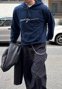 Ναυτικό φούτερ με λευκή εκτύπωση γραφής, φορεμένο με μαύρες cargo παντελόνες που διαθέτουν μεταλλική αλυσίδα. Δερμάτινο μπουφάν ριγμένο σ�τον έναν ώμο.