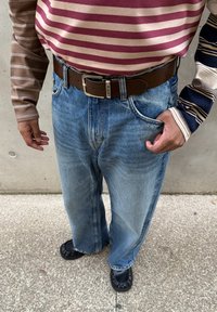 Koszula na długi rękaw w paski w kolorze bordowym i brązowym, zestawiona z jasnoniebieskimi, luźnymi dżinsami i brązowym paskiem; czarne buty wsuwane.