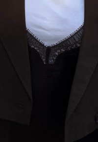 Blazer nero sopra una maglietta bianca con scollatura a V bordata in pizzo. Il pizzo presenta motivi intricati con dettagli frangianti sul collo.