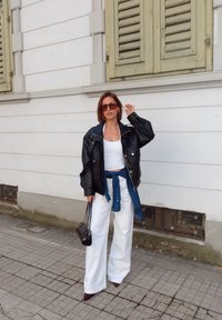 Veste surdimensionnée en cuir noir, débardeur blanc, pantalon large blanc, jean bleu noué à la taille, lunettes de soleil foncées et petit sac à main noir.
