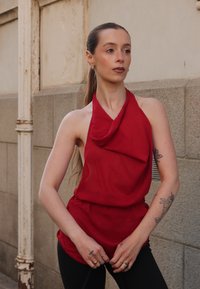 Rotes Oberteil im Halter-Stil, mit drapiertem Stoff, lockerem Schnitt und leichtem Material. Kombiniert mit schwarzen Hosen, die ein lässiges, aber dennoch markantes Design präsentieren.