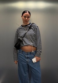 Fekete-fehér csíkos, rövidített hosszú ujjú ing, világoskék bő szárú farmernadrág, fekete oldaltáska, fehér okostelefon és fülhallgató.