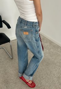 Jeans de mezclilla de color azul claro con un corte relajado, que cuentan con una etiqueta marrón en el bolsillo trasero, remaches de cobre y puños doblados.