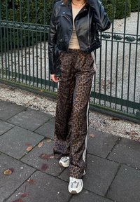 Chaqueta de motorista de cuero negro, top beige y pantalones anchos de estampado leopardo marrón con rayas laterales blancas; combinados con zapatillas claras.