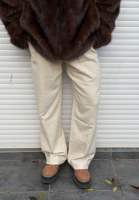 Cappotto in pelliccia sintetica marrone, pantaloni beige con motivo a quadri e stivali marroni con suola in gomma nera. Materiali testurizzati e stratificati.