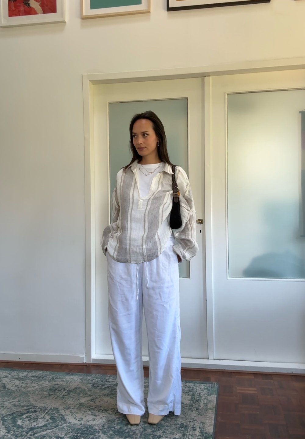 Cămașă din in cu dungi, de culoare deschisă, purtată peste un tricou alb; asociată cu pantaloni largi din in alb. Design simplu cu o croială lejeră.