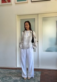 Cămașă din in cu dungi, de culoare deschisă, purtată peste un tricou alb; asociată cu pantaloni largi din in alb. Design simplu cu o croială lejeră.