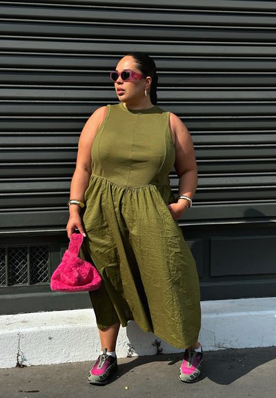 Vestido sin mangas de color verde oliva con un torso ajustado y una falda fluida, combinado con un bolso fluffy rosa y zapatillas deportivas grises y rosas.