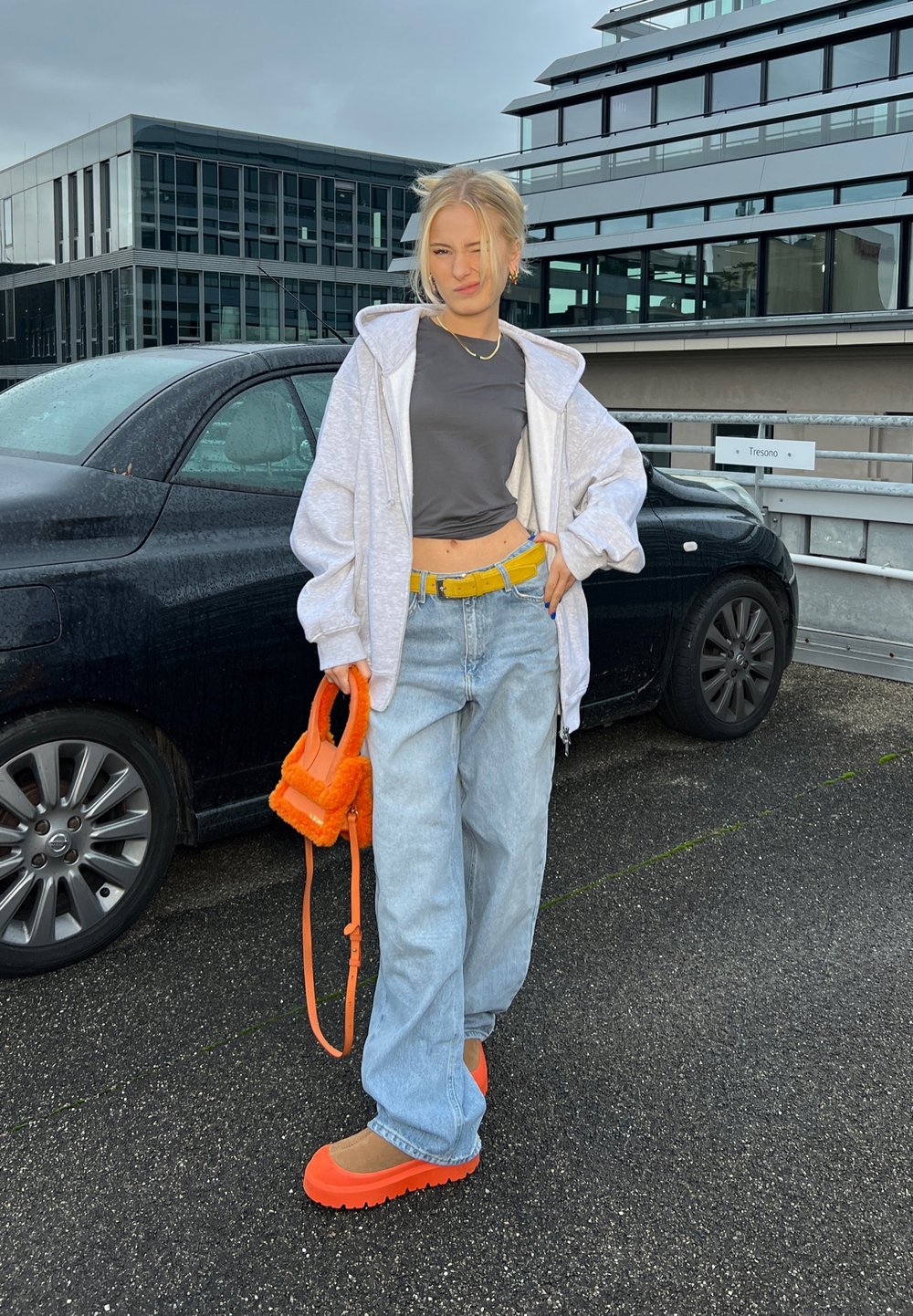 Un conjunto informal que incluye una sudadera gris claro, una camiseta corta gris oscuro, unos vaqueros anchos azul claro, un cinturón amarillo, y zapatos y bolso naranja brillante.