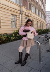 Rožinė dryžuota marškinėlių viršuje, dėvimi ant rudos palaidinės, smėlio spalvos sijonas, raštuotos pėdkelnės ir juodi aukšti batai iki kelių. Laiko baltą purų maišą.