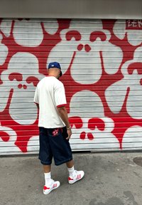 White t-shirt with red accents, blue denim shorts, and red and white trainers. The background features a red and white monkey graphic pattern.