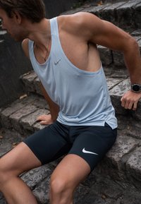 Hele sinine sääreline sporditopp ja mustad sobivad lühikesed püksid, millel on Nike logo aktsendid. Topil on vabam istuvus ja sile tekstuur.