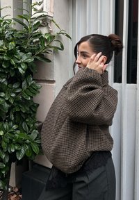 Braune Hahnentritt-Übergröße-Jacke mit hohem Kragen, die eine dezente Textur und ein geschichtetes Design aufweist, kombiniert mit dunkelgrauen Hosen.