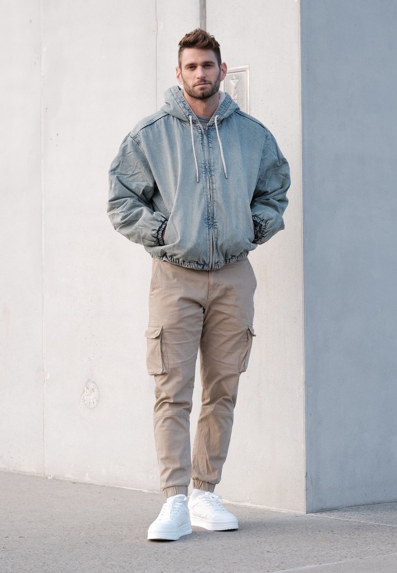 Veste à capuche en denim bleu clair, pantalons cargo beiges et baskets blanches. Comprend des poignets et une ceinture élastiques, avec des poches cargo sur les pantalons.