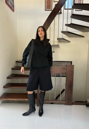 Sudadera negra sobredimensionada, pantalones cortos negros holgados, botas negras hasta la rodilla y una bolsa de hombro. Diseño simple, color uniforme y textura suave.