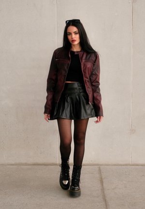 Chaqueta de cuero burdeos con cremalleras, top corto negro, falda de cuero negra acampanada, medias negras y botas negras de suela gruesa con acentos metálicos.