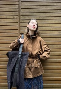 Brun jakke i semsket skinnlignende materiale med glidelåsfeste i kragen og snor i midjen. Svart quiltet totebag med teksturert overflate og justerbar stropp.