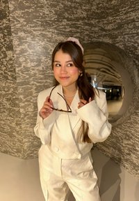 Biały, teksturowany garnitur z dużą marynarką i spodniami, zdobiony kwiatową haftem. Dodatki to naszyjnik z pereł i okulary przeciwsłoneczne.