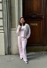 Vaaleanpunainen vapaa-ajan asukokonaisuus, jossa on pitkät hihat ja nyöritettävät housut, yhdistettynä harmaaseen, pörröiseen liiviin. Hopeiset, kärkikuvioiset kengät ja kahvikuppi.