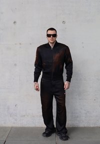 Μαύρο bomber jacket με καφέ λεπτομέρειες, κλείσιμο με φερμουάρ και ριμπ μανσέτες, συνδυασμένο με μαύρο παντελόνι και χοντρές μαύρες αθλητικές σόλες.