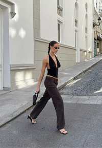Top negro con cuello halter, pantalones de pierna ancha marrón oscuro, bolso negro y sandalias de tacón abierto. Texturas suaves y una silueta moderna.