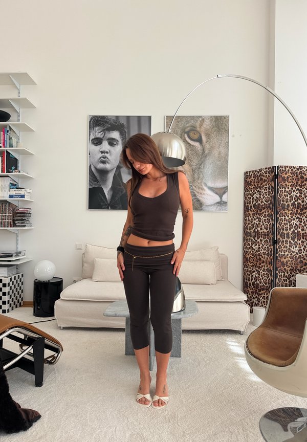Kvinde i sort ærmeløs top og leggings, stående i en moderne stue med beige sofa, leopardprint skærm og store portrætter af løve og mand.