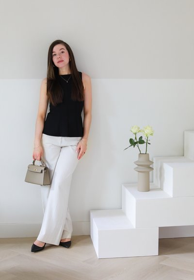 Top negro sin mangas combinado con pantalones de pierna ancha de color beige claro. Sosteniendo un pequeño bolso beige. Dos rosas blancas en un jarrón beige en los escalones.