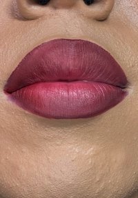 Mattes Lippenstift in einem Farbverlauf von tiefem Pink zu Burgunderrot. Die Lippen sind voll mit sichtbarer Textur und feinen Linien, vor einem glatten, helleren Hautton-Hintergrund.