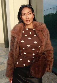 Brun prickig klänning, brun fuskpälsjacka och brun pälsväska. Texturerat tyg, figursydd design, bärs med svart läderkjol.