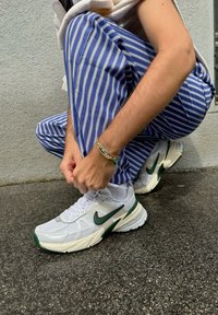 Valged Nike võrgusilma tossud roheliste aktsentidega, tekstuuriga mustrid ja paks tall. Kandja kohendab paelu kükkides.