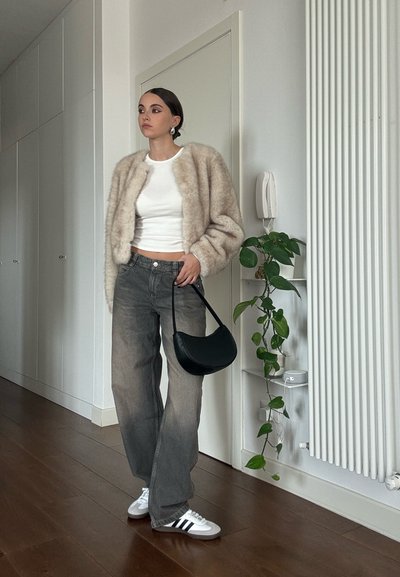 Chaqueta de peluche beige corta, camisa blanca ajustada, vaqueros grises de pierna ancha, bolso negro de hombro, zapatillas blancas con rayas negras, ambiente interior.