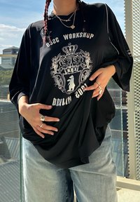 T-shirt preta oversized com um design gráfico apresentando uma coroa e um urso, feita de um tecido macio, combinada com uns jeans azul claro.