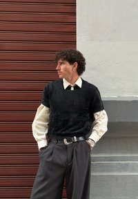 Zwart gestructureerd kortärmelig truitje, gedragen over een wit overhemd met kraag, gecombineerd met grijze, hooggesneden broek en een zilveren riem.