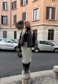 Czarna skórzana kurtka bomberka, czarny golf, teksturowana miętowa spódnica, czarne kozaki do kolan, mała czarna torebka, miejskie tło.