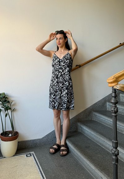Vestido de estampado floral en blanco y negro con tirantes ajustables, largo hasta la rodilla y una ligera forma de A. Sandalias marrones completan el look.