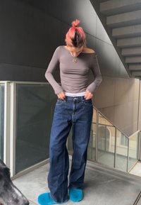 Top gris de manga larga, jeans azul relajados, y zapatillas de casa azules brillantes. Cintura de Calvin Klein visible, tejido suave y textura blanda.