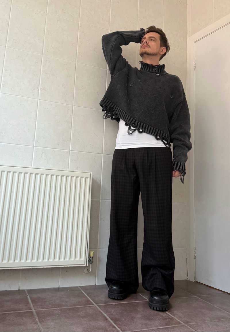 Grå cropped sweater med ribbet kant og frynsete kanter, kombineret med løse sorte ternede bukser og chunky sorte plateau sko.
