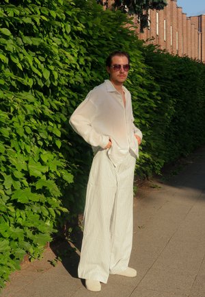 Camisa de lino blanca, ligera y de corte holgado con cuello, combinada con pantalones anchos a rayas en crema y blanco. Accesorios incluyen unas gafas de sol.