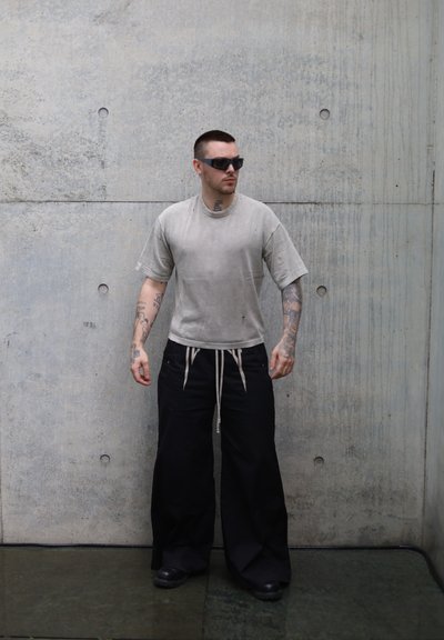 Camiseta de gran tamaño de color gris claro con mangas cortas, combinada con pantalones anchos negros con cuerdas. Texturas suaves, acentos mínimos.