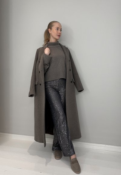 Abrigo largo gris sobre un suéter gris, combinado con pantalones de lentejuelas plateadas brillantes y mocasines marrones. Texturas suaves y diseño casual.