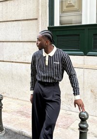 Czarna i biała w paski długosleeve polo z beżowym kołnierzykiem, zestawiona z wysokimi czarnymi spodniami; obie cz�ęści mają luźny krój i gładką teksturę.