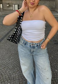 Top bianco senza spalline, jeans a palazzo azzurri chiari con borchie argentate e una borsa nera decorata con grandi borchie argentate. Accessori casual visibili.
