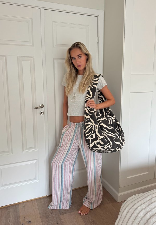 Woman standing indoors wearing a gray crop top, striped wide pants, holding a large black and white zebra print tote bag on her shoulder.