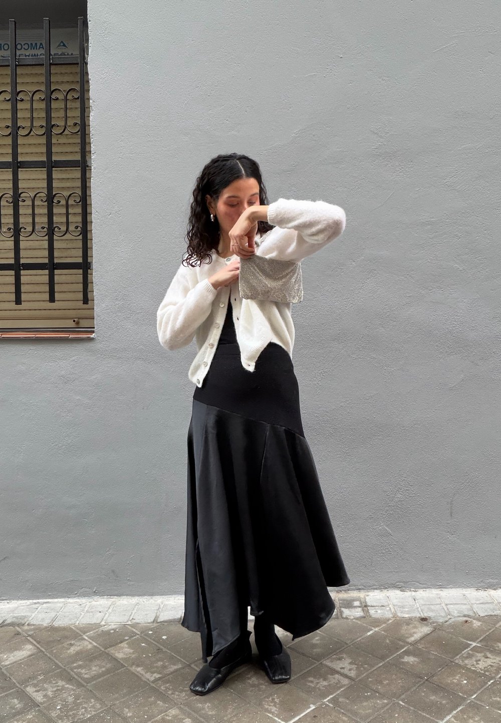 Valge kootud kardigan musta varrukatuta kleidi üle, millel on laiendatud serv. Komplekti kuuluvad mustad kingad ja hõbedane tekstuuriga käekott.