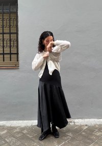 Valge kootud kardigan musta varrukatuta kleidi üle, millel on laiendatud serv. Komplekti kuuluvad mustad kingad ja hõbedane tekstuuriga käekott.