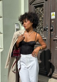 Bodysuit de padrão leopardo preto combinado com calças brancas de cintura alta. Blazer bege pousado sobre o ombro. Bolsa bordô e joias prateadas.
